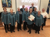 Ansiomerkkien saajat 2-vuotismerkistä 50-vuotismerkkiin. Kuoron puheenjohtajalle, kirkkomusiikkipiirin sihteerille Leila Kotamäelle luovutettiin kirkkomusiikkiliiton myöntämä kuorolaisen erityisansiomerkki, joka myönnetään erityisistä ansioista kirkkomusiikin hyväksi tehdystä työstä. 